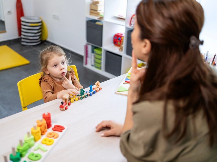 Young child watching a therapist model mouth movements during childhood apraxia of speech therapy in Apple Valley, CA